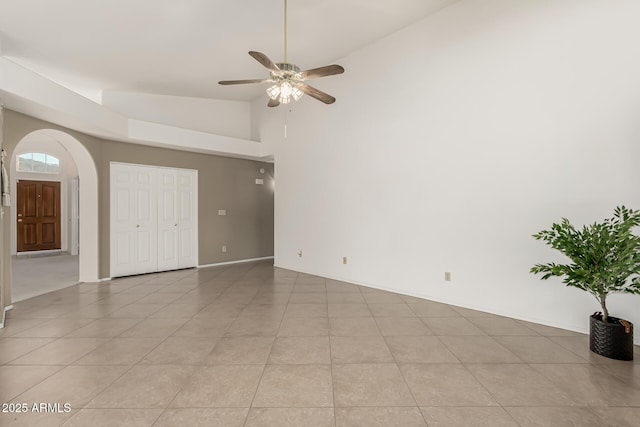 interior space with arched walkways, light tile patterned floors, ceiling fan, high vaulted ceiling, and baseboards