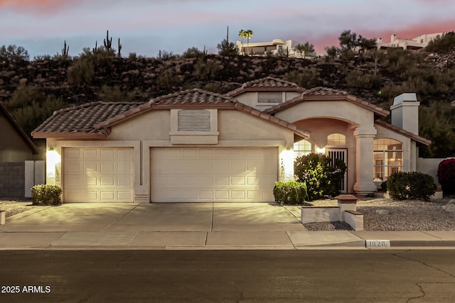 mediterranean / spanish-style house with concrete driveway, an attached garage, a tiled roof, and stucco siding