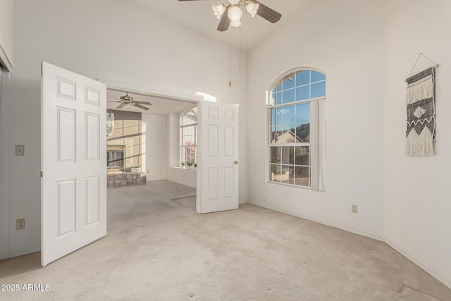 unfurnished room with high vaulted ceiling, light carpet, ceiling fan, and a stone fireplace