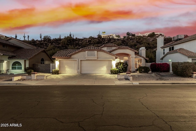 mediterranean / spanish-style home with a garage, fence, concrete driveway, a tiled roof, and stucco siding