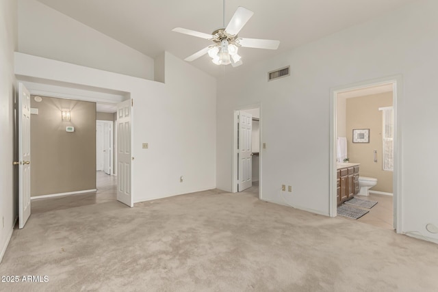 unfurnished bedroom with visible vents, light colored carpet, ensuite bath, a walk in closet, and high vaulted ceiling