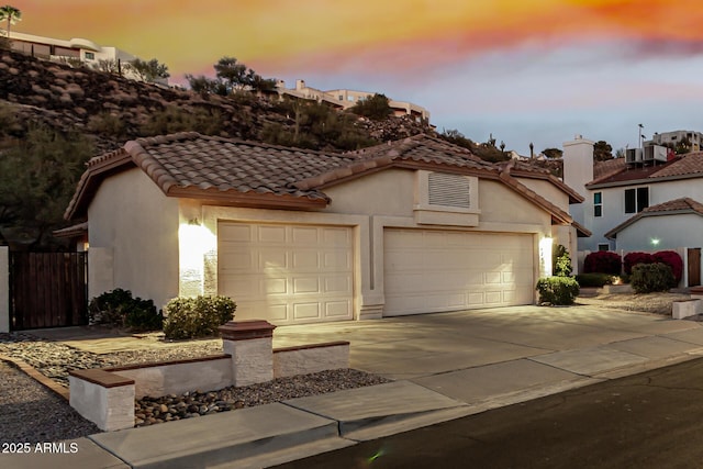 mediterranean / spanish-style house featuring concrete driveway, an attached garage, a tiled roof, and stucco siding