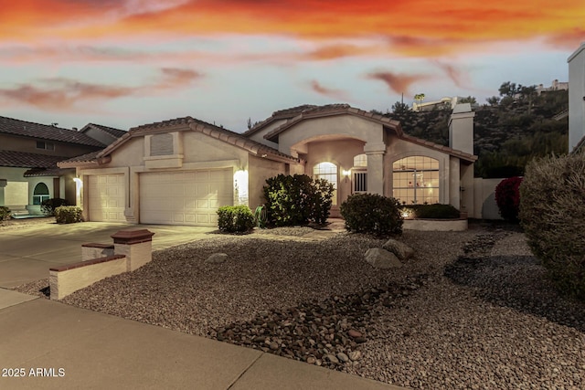 mediterranean / spanish-style house featuring a garage, driveway, a chimney, and stucco siding