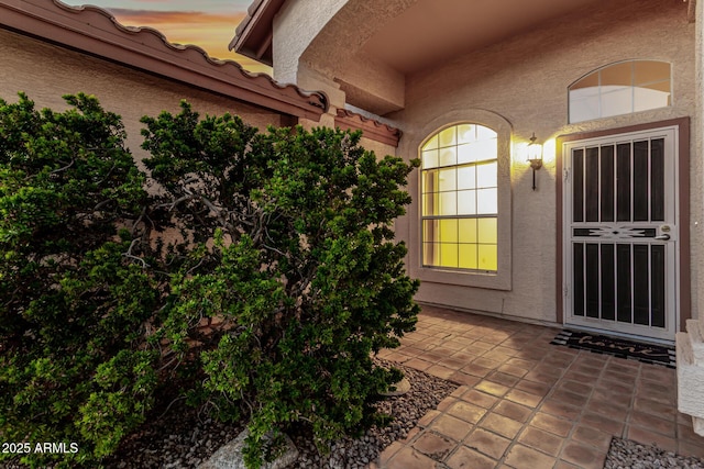 view of exterior entry with a patio area, a tile roof, and stucco siding