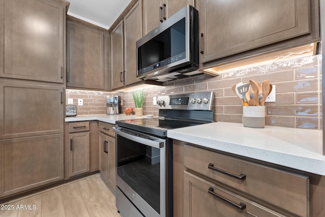 kitchen featuring stainless steel appliances, backsplash, light wood-style flooring, and light stone countertops