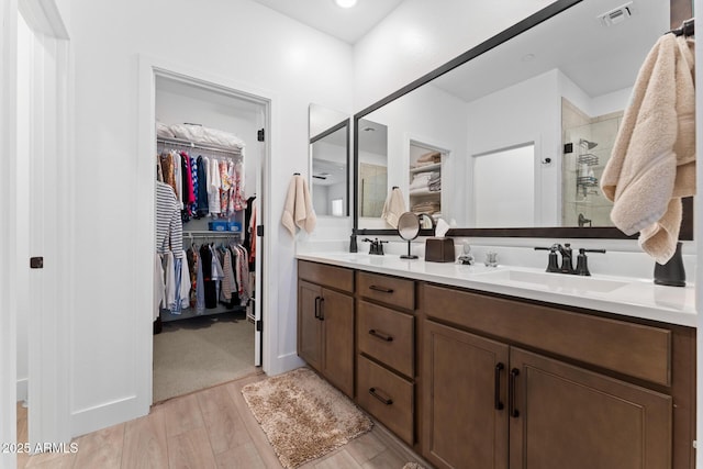 full bathroom with double vanity, visible vents, wood finished floors, a spacious closet, and a sink