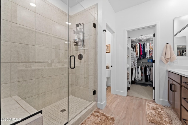 bathroom featuring baseboards, wood finished floors, a spacious closet, vanity, and a shower stall