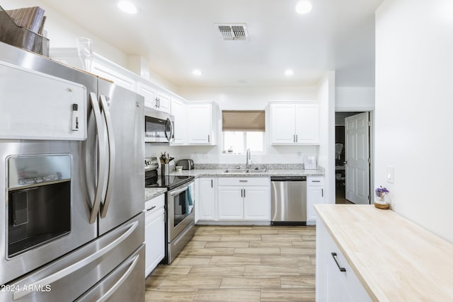 kitchen with white cabinets, sink, light stone countertops, appliances with stainless steel finishes, and light hardwood / wood-style floors