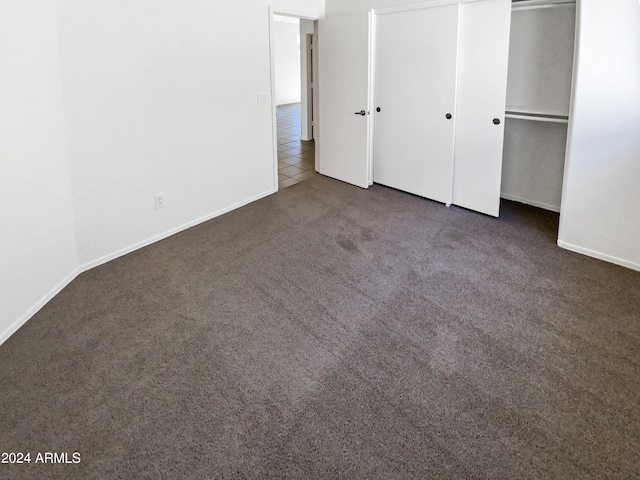 unfurnished bedroom with dark carpet and a closet