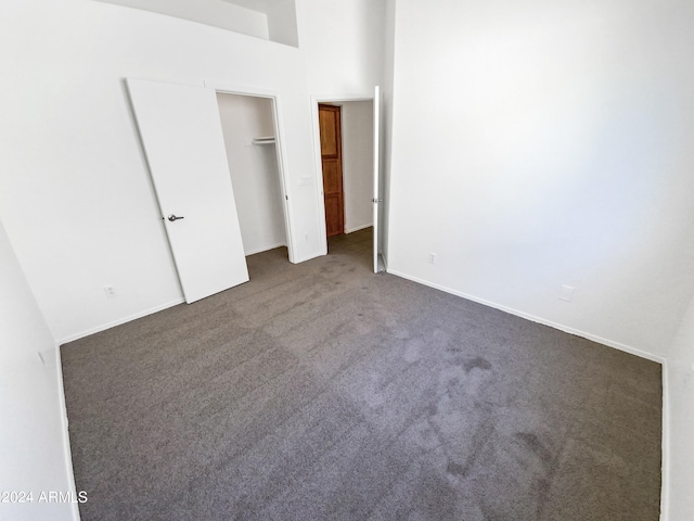 unfurnished bedroom featuring dark colored carpet and a towering ceiling