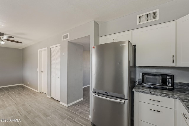 kitchen featuring freestanding refrigerator, black microwave, a ceiling fan, light wood-style floors, and white cabinetry