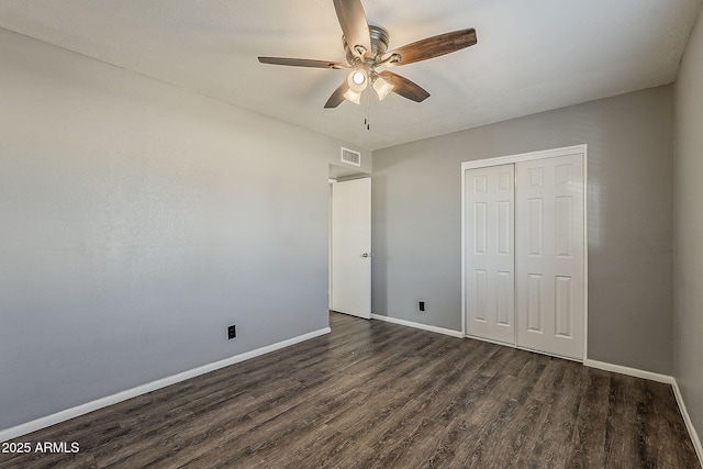 unfurnished bedroom featuring dark wood-style floors, a closet, baseboards, and a ceiling fan