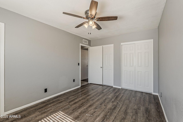 unfurnished bedroom with multiple closets, dark wood-style floors, baseboards, and a ceiling fan