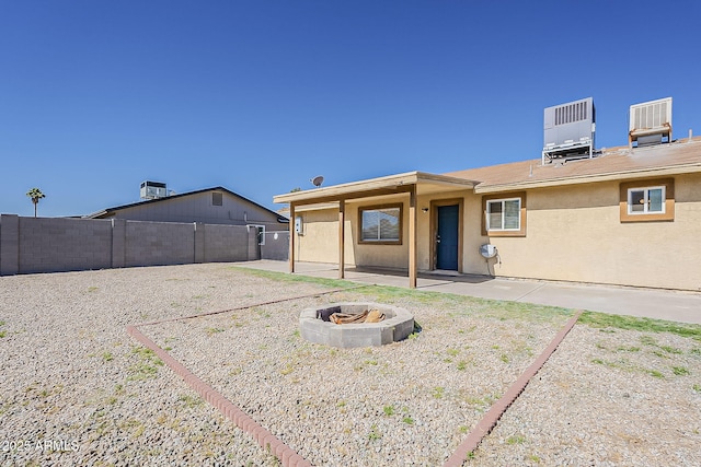 rear view of property featuring a fire pit, a patio, a fenced backyard, cooling unit, and stucco siding