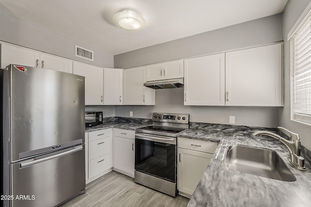 kitchen featuring stainless steel appliances, a sink, under cabinet range hood, white cabinetry, and light wood-style floors