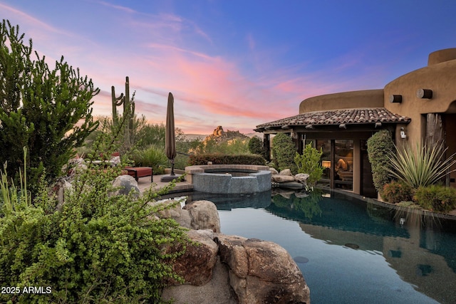 pool at dusk with an in ground hot tub