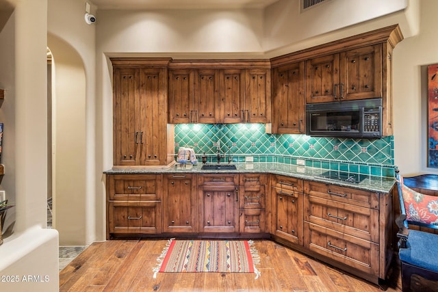 kitchen featuring sink, light hardwood / wood-style flooring, black appliances, and light stone countertops