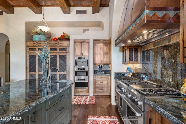 kitchen with sink, dark stone countertops, appliances with stainless steel finishes, dark hardwood / wood-style flooring, and beam ceiling