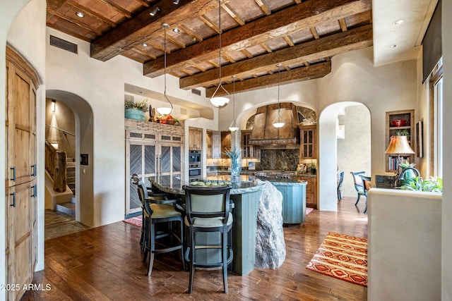 kitchen with pendant lighting, a breakfast bar area, a center island, dark wood-type flooring, and beam ceiling