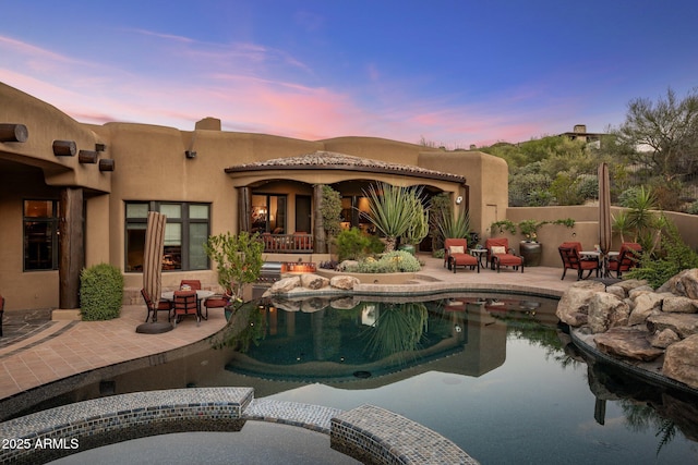 pool at dusk with a patio and an in ground hot tub