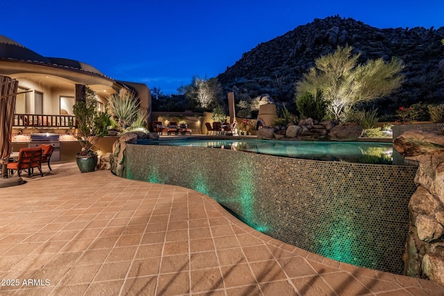 view of pool featuring an outdoor kitchen, a fireplace, a mountain view, and a patio