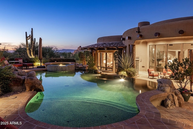 pool at dusk with an in ground hot tub and a patio area