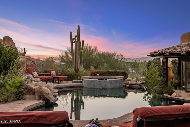 patio terrace at dusk featuring a swimming pool with hot tub and a mountain view