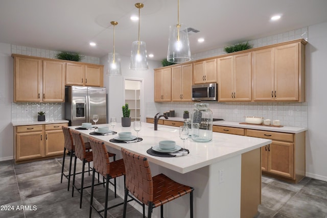 kitchen with light brown cabinets, an island with sink, decorative light fixtures, and appliances with stainless steel finishes