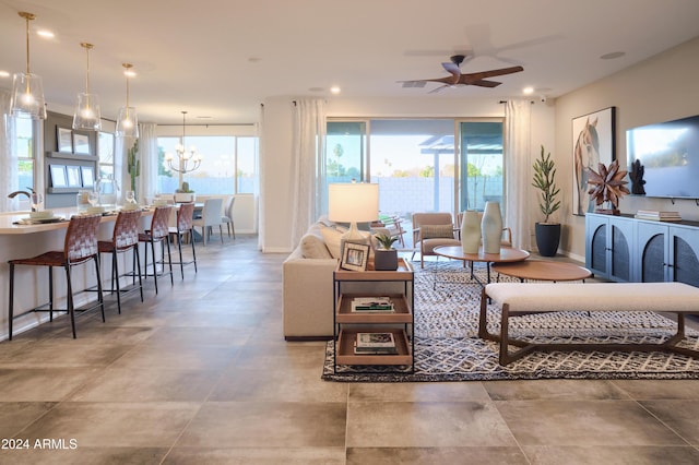 living room with ceiling fan with notable chandelier, sink, and a wealth of natural light