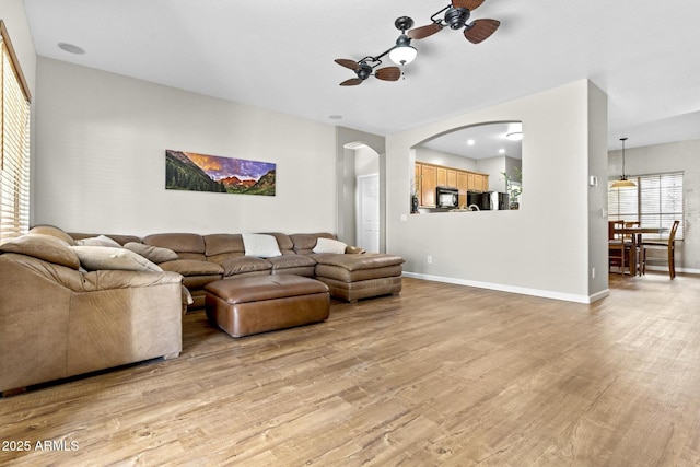 living room with ceiling fan, light wood finished floors, arched walkways, and baseboards