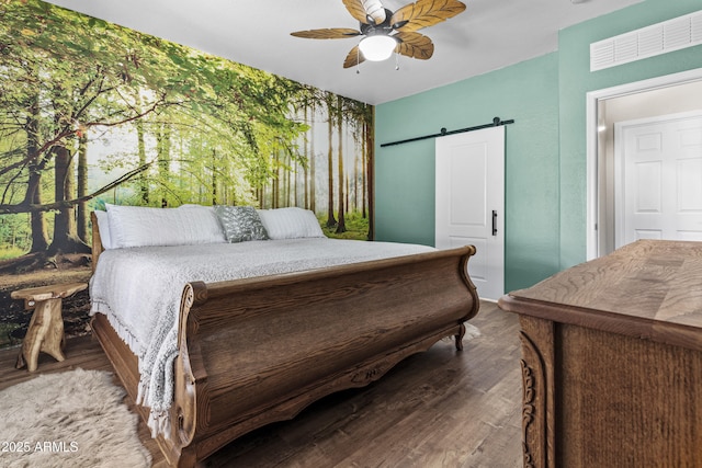 bedroom with a barn door, visible vents, ceiling fan, and wood finished floors