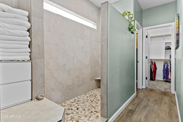 bathroom with a walk in closet, wood finished floors, baseboards, and walk in shower