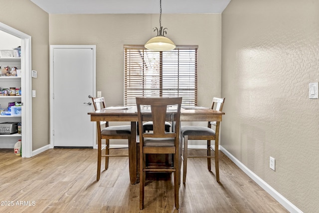 dining area featuring a textured wall, light wood-type flooring, and baseboards