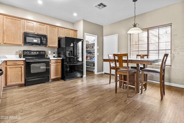 kitchen featuring visible vents, light wood-style flooring, hanging light fixtures, light countertops, and black appliances