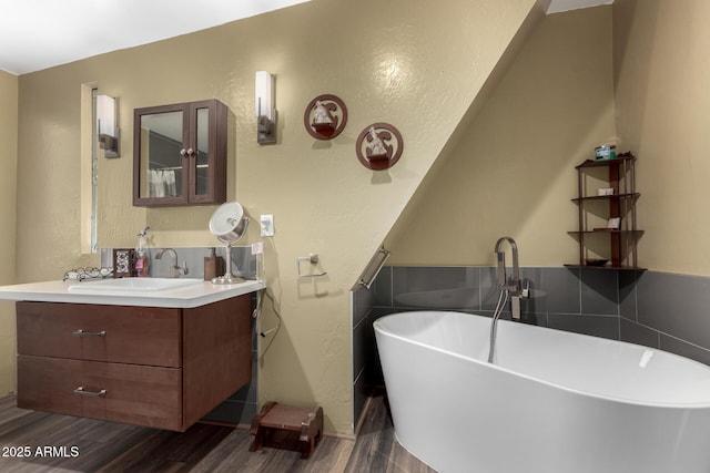 bathroom featuring a textured wall, a freestanding bath, vanity, and wood finished floors