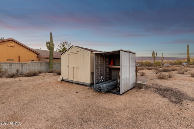 outdoor structure at dusk featuring a shed, fence, and an outdoor structure