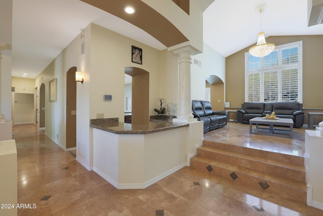 kitchen featuring ornate columns, decorative light fixtures, dark stone countertops, a chandelier, and lofted ceiling