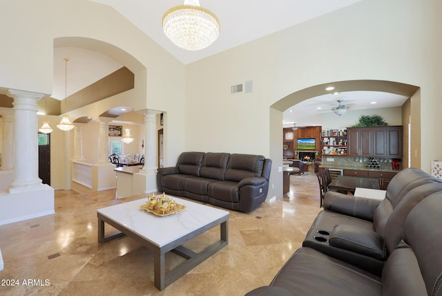 living room featuring ceiling fan with notable chandelier, ornate columns, and high vaulted ceiling