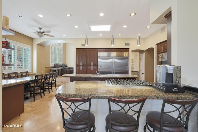 kitchen with ceiling fan, sink, light stone counters, pendant lighting, and appliances with stainless steel finishes