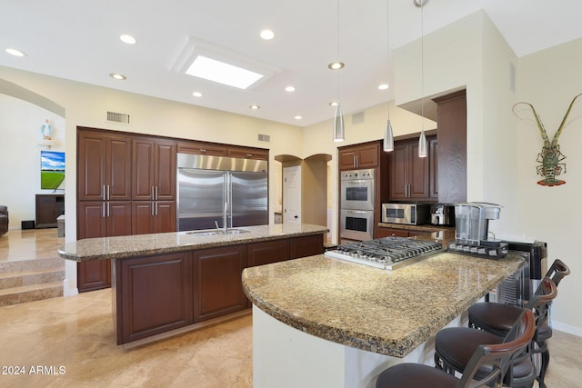 kitchen featuring decorative light fixtures, stone countertops, stainless steel appliances, and an island with sink