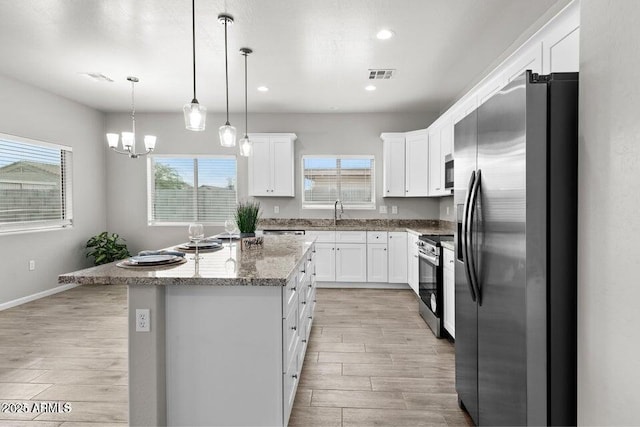 kitchen featuring a kitchen island, stainless steel appliances, white cabinets, and hanging light fixtures