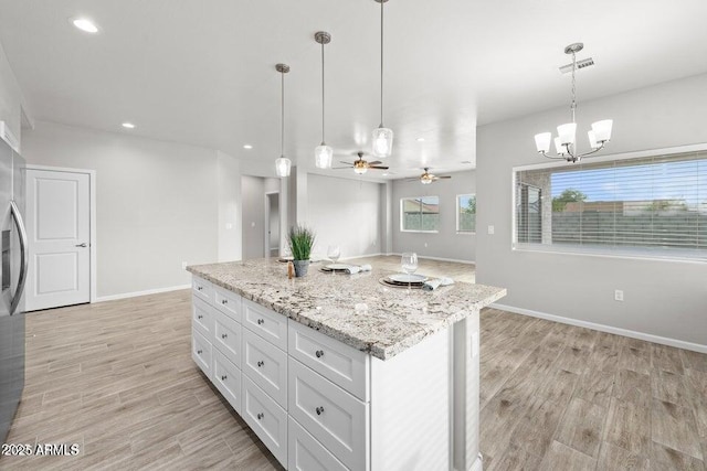 kitchen with hanging light fixtures, light stone countertops, a kitchen island, white cabinets, and ceiling fan with notable chandelier