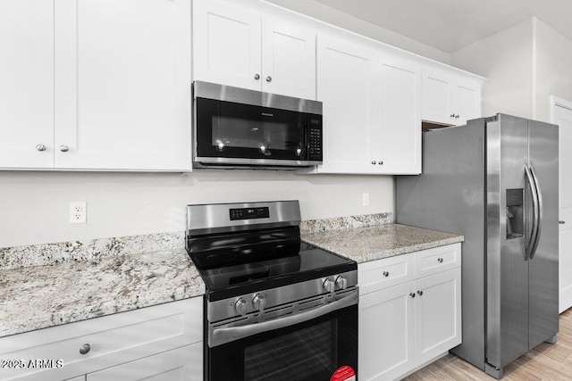 kitchen with white cabinets, stainless steel appliances, light hardwood / wood-style floors, and light stone counters