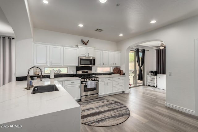 kitchen with light wood finished floors, arched walkways, white cabinets, stainless steel appliances, and a sink