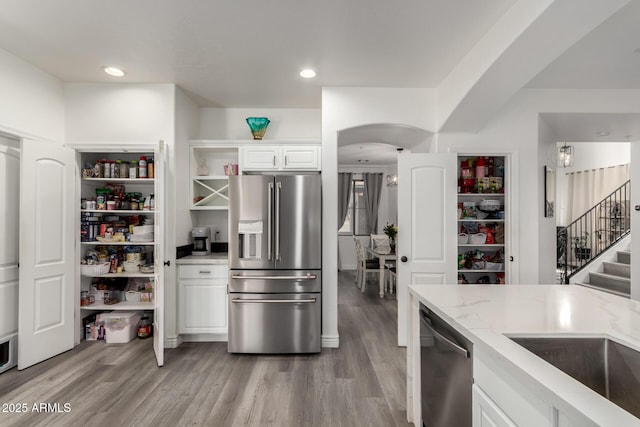 kitchen featuring light wood-type flooring, light stone countertops, appliances with stainless steel finishes, and white cabinets