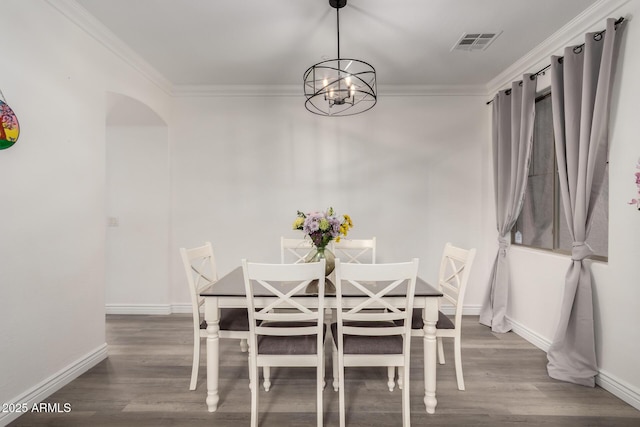 unfurnished dining area featuring wood finished floors, visible vents, baseboards, arched walkways, and crown molding