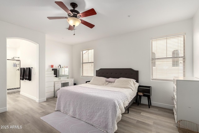 bedroom with light wood-type flooring, arched walkways, and baseboards