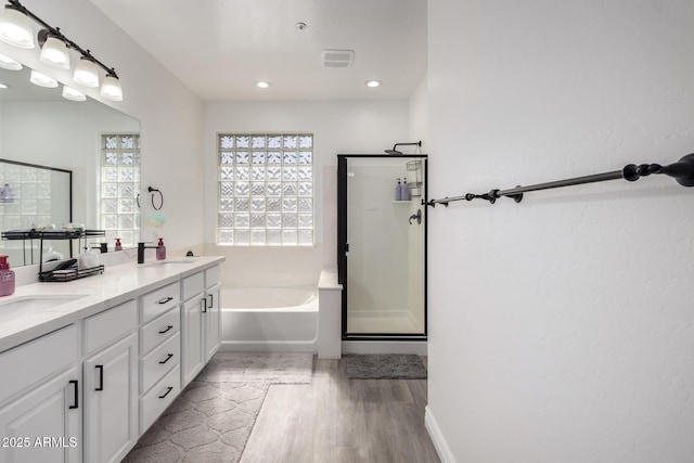 bathroom featuring wood finished floors, double vanity, a stall shower, a sink, and a garden tub