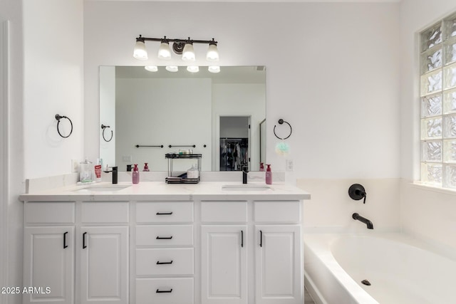 full bath featuring double vanity, a spacious closet, a garden tub, and a sink