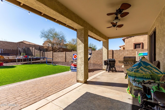 view of patio featuring a trampoline, a fenced backyard, grilling area, and ceiling fan